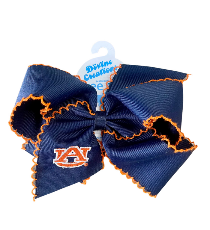 A navy hair bow with orange embroidered moon stitches and a logo on the bottom, attached to a blue and white cardboard backing.