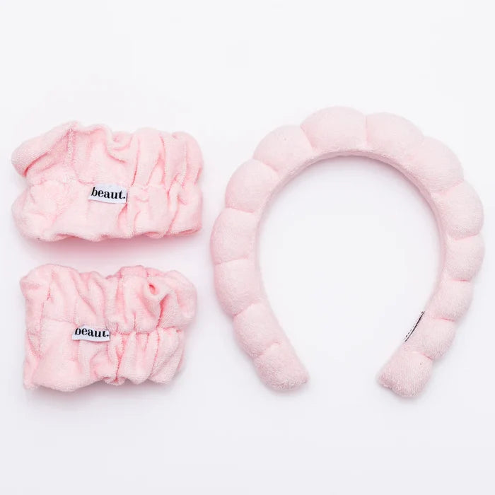 A set of light pink terrycloth headband and wristbands, with the word 'beaut' written on them.