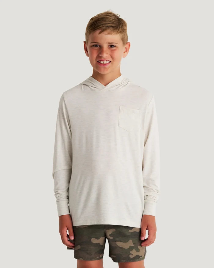 Young boy standing in front of a white background wearing a white and beige hoodie and camo shorts.
