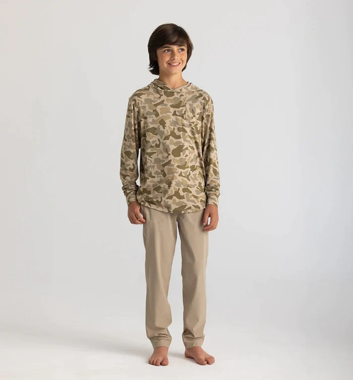 Person wearing a camouflage hoodie and beige pants on a white background