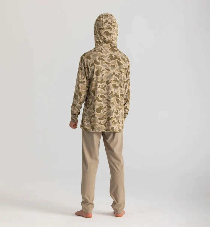 Person wearing a camouflage hoodie and beige pants on a white background