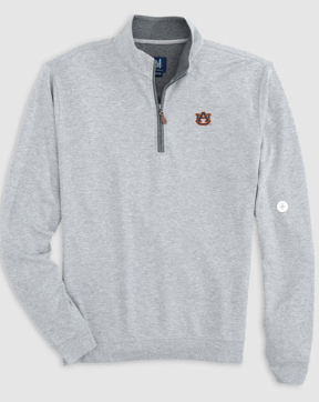 A boy wearing a long sleeve blue pullover with a 1/4 zip and a logo on the chest, paired with beige pants, standing against a white wall.