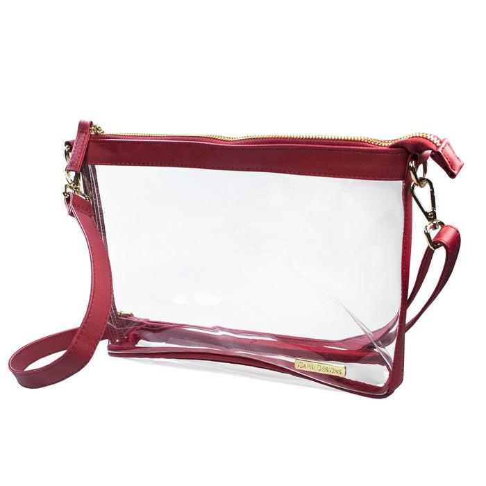 A clear plastic pouch bag with burgundy red faux leather trim, zipper, and strap, featuring a small gold brand plaque on the bottom right.