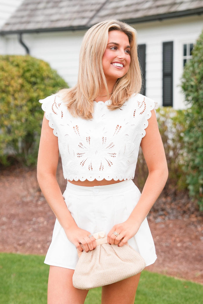 Woman in a white outfit holding a beige clutch in front of a house.