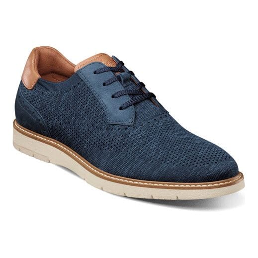 A casual men's shoe with a navy blue knit textile upper and nubuck detailing, featuring a white rubber outsole and tan accents.