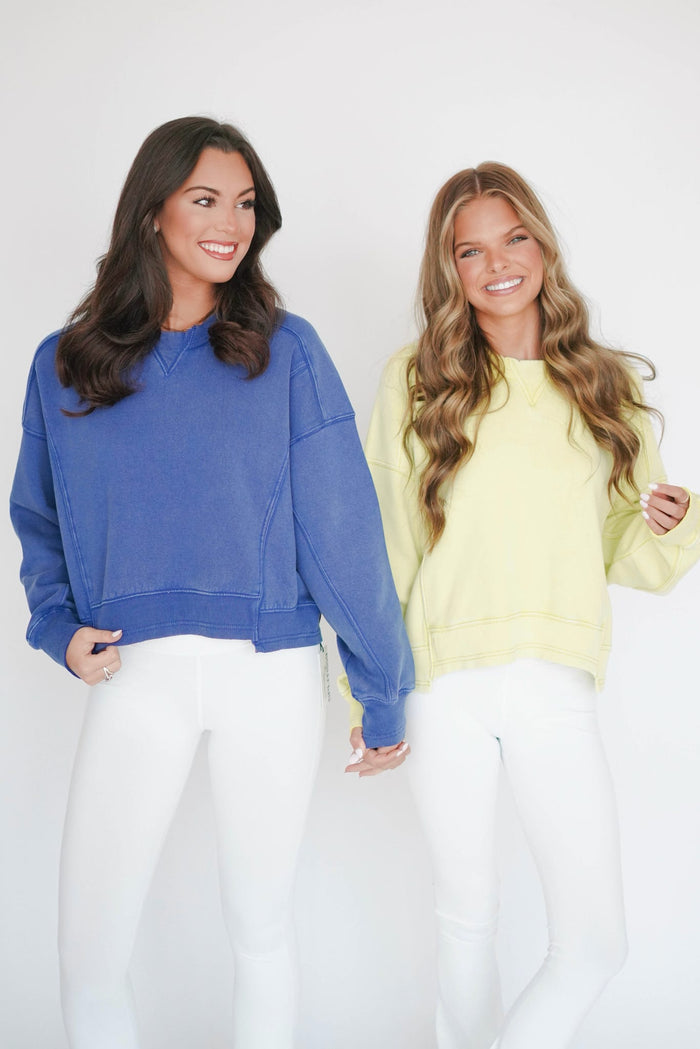 Two women wearing blue and yellow sweatshirts with white pants against a white background