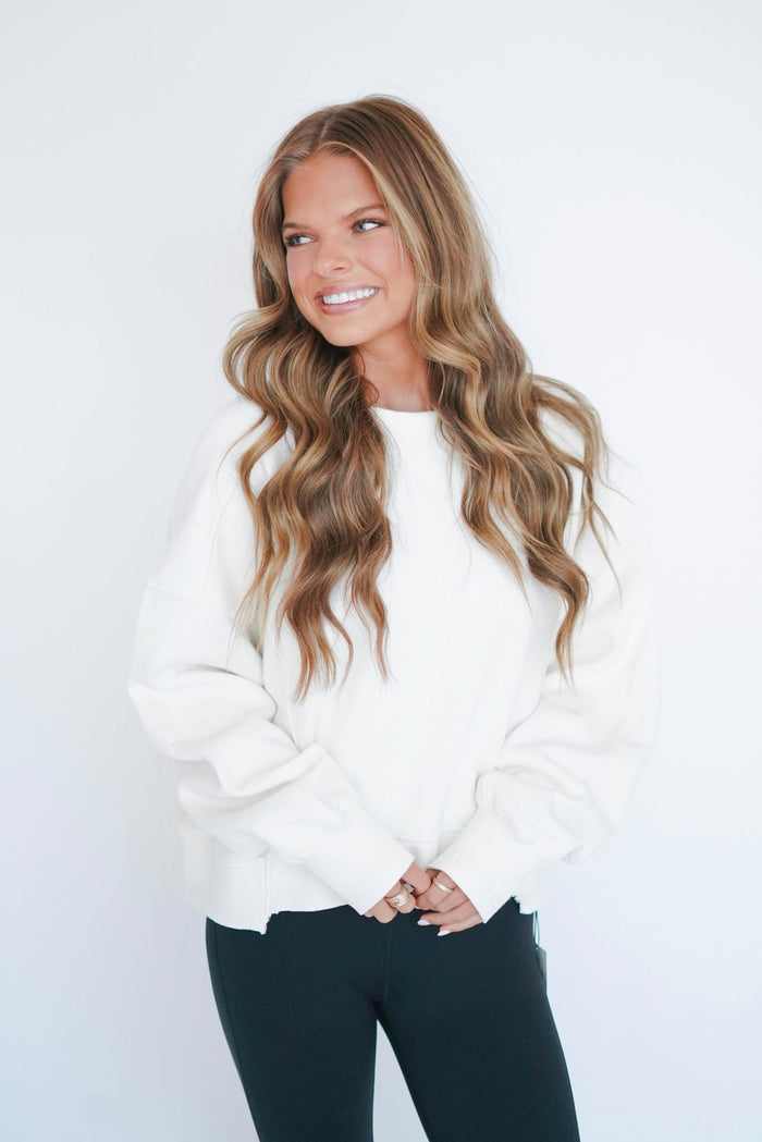 Woman wearing a white sweater and black pants against a plain background