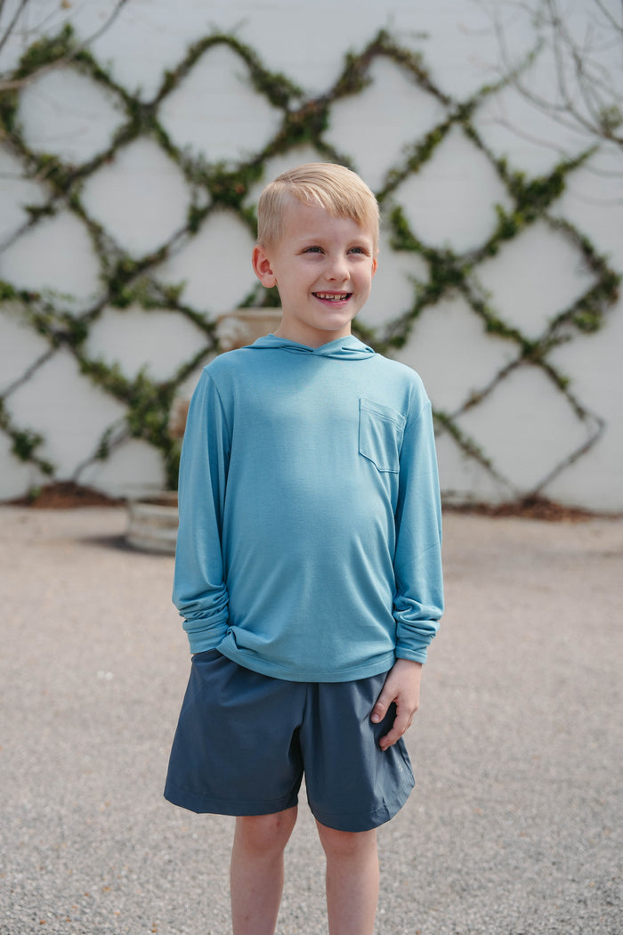 Young boy in blue shirt and shorts standing outdoors with wooden slats in the background