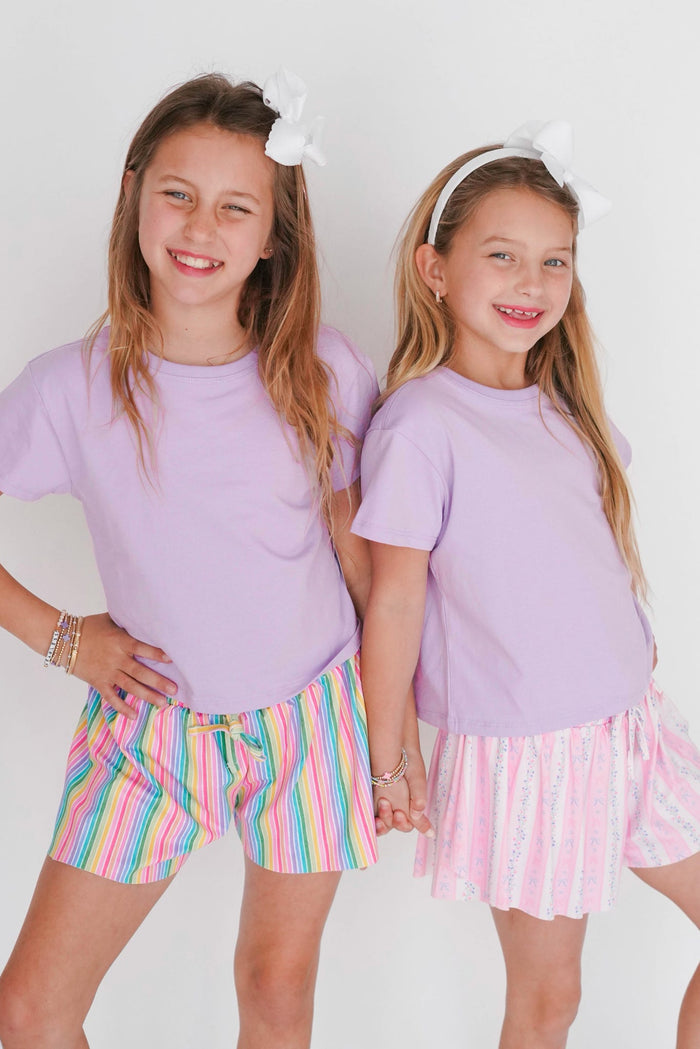 Two young girls wearing matching purple tops and colorful shorts on a white background