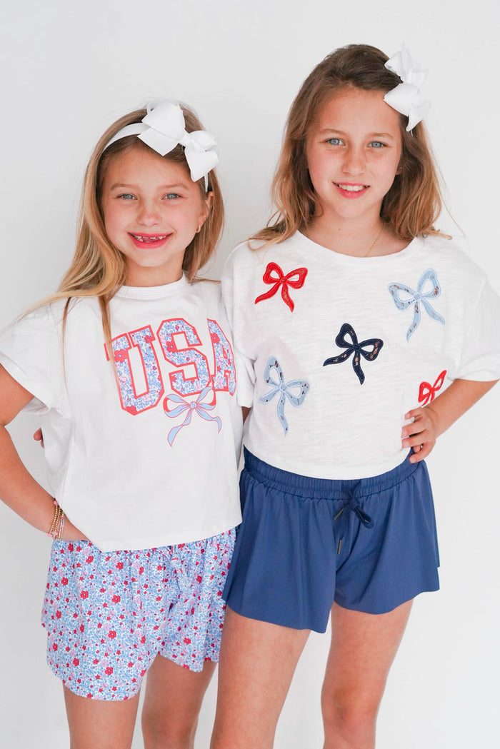 Two young girls wearing matching outfits with bows and 'USA' text on a white background