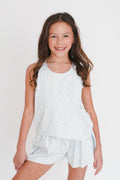 Young girl wearing a white sleeveless top and shorts set on a plain background