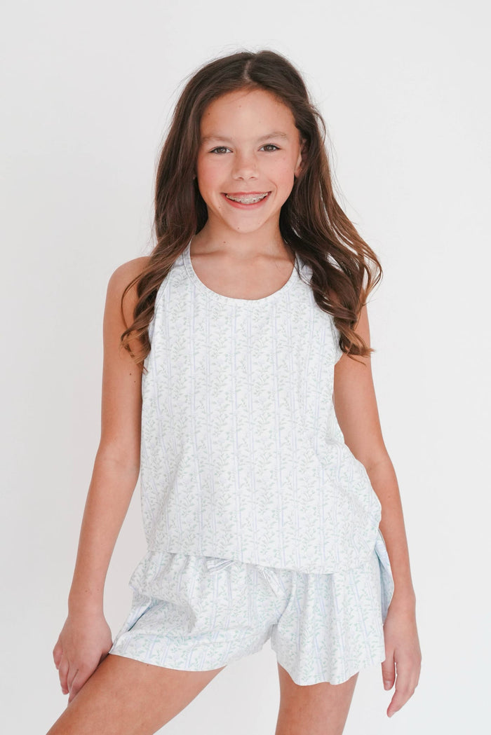 Young girl wearing a white sleeveless top and shorts set on a plain background