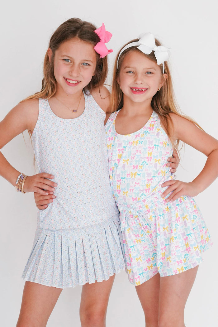 Two young girls posing together wearing light blue and floral outfits against a white background
