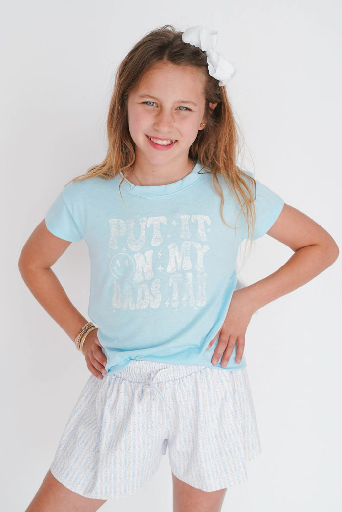 Young girl wearing a light blue t-shirt with text and white shorts on a plain background