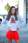 Girl wearing a gray sweatshirt with a logo and a red skirt standing on a sidewalk.