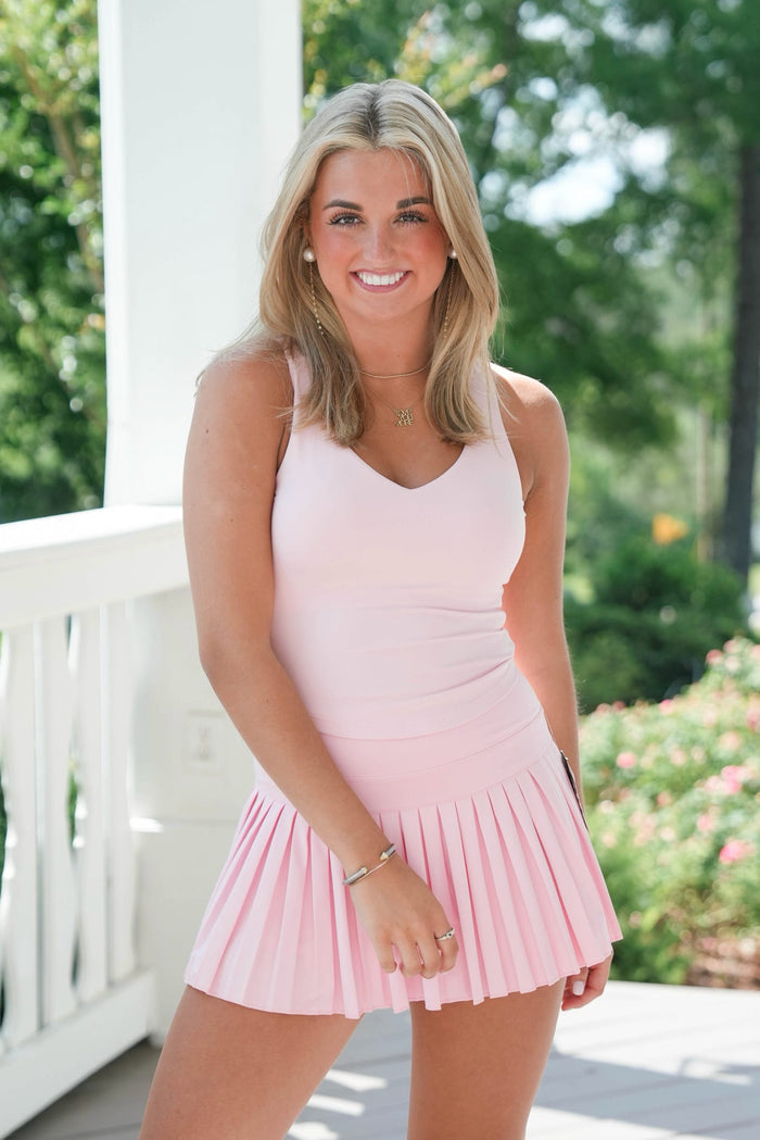Woman in a pink dress standing on a porch with greenery in the background