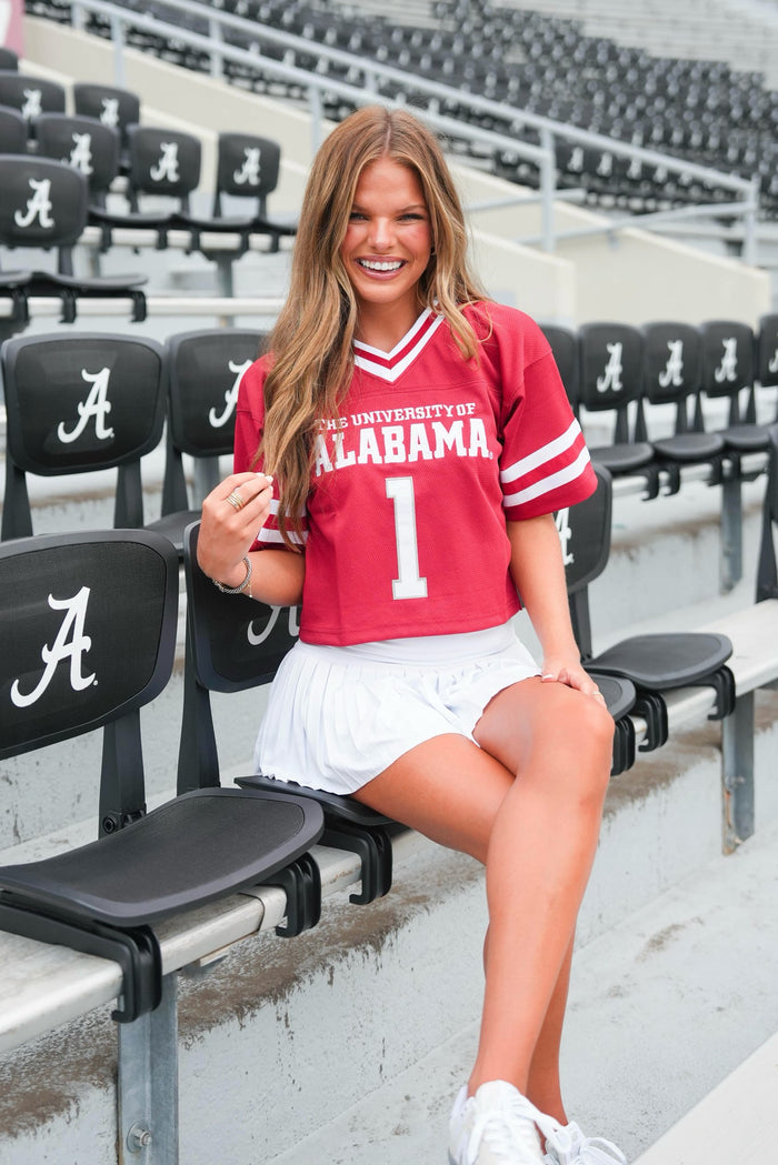 Woman in a red 'University of Alabama' jersey sitting in stadium seats.