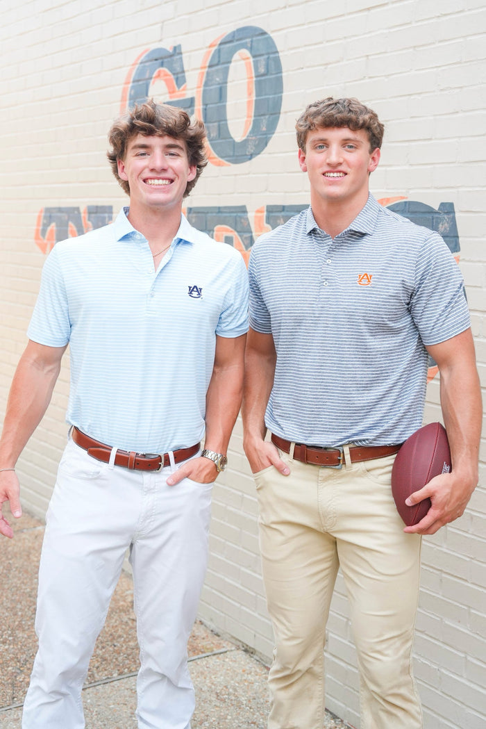 Two men standing in front of a wall with 'GO' and 'Auburn' text, one holding a football.