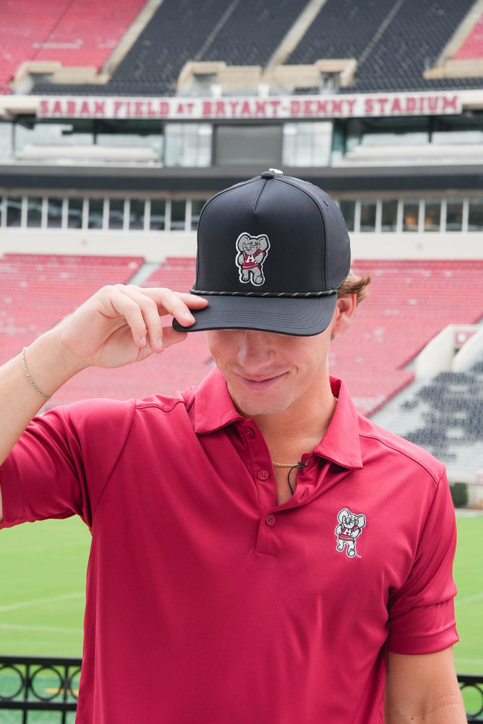 Person wearing a black cap with a logo and red polo shirt in front of a stadium.