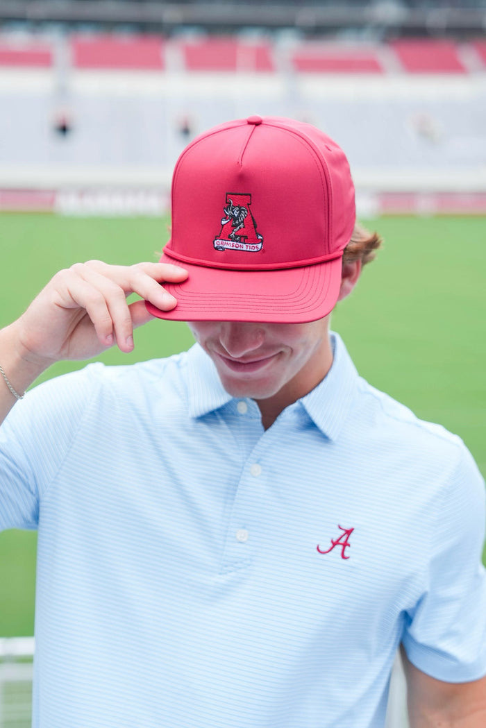 Person wearing a red cap with a logo and light blue shirt with a logo, standing on a grassy field.