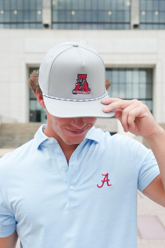 Person wearing a white cap with a logo and a light blue polo shirt with a red logo, standing in front of a building.