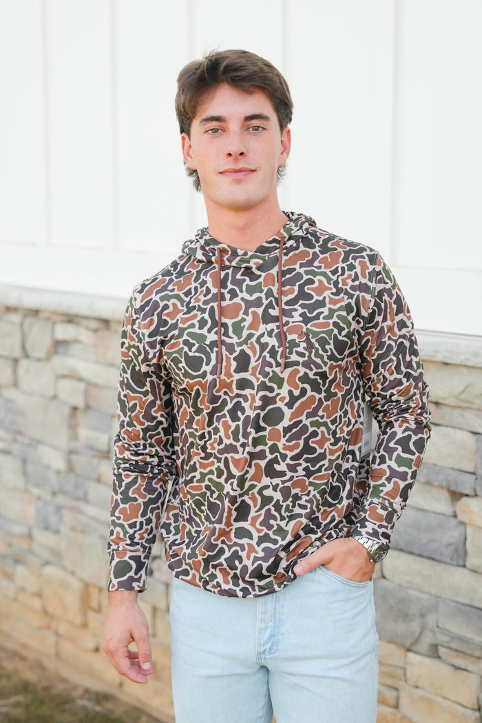 Man wearing a patterned hoodie standing against a stone wall.