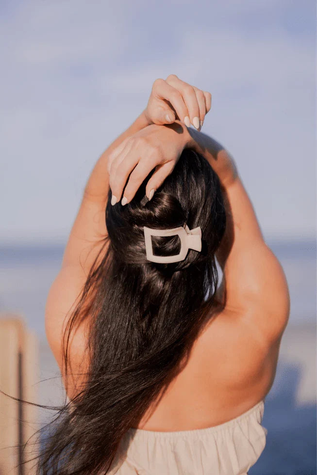 Woman posing with a beige open flat hair clip holding her hair half up, half down.