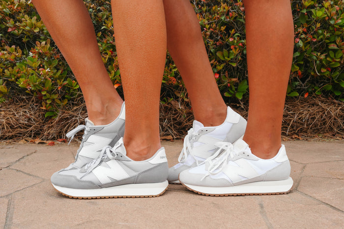 Two pairs of feet wearing white and gray sneakers on a stone surface with greenery in the background.