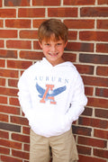 Youth wearing a white hoodie with 'AUBURN' text and a logo on the front standing against a brick wall.