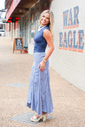 A woman modeling a sleeveless navy blue top and a matching blue-and-white gingham maxi skirt, standing on a sidewalk next to a white brick wall with 'WAR EAGLE' painted on it.